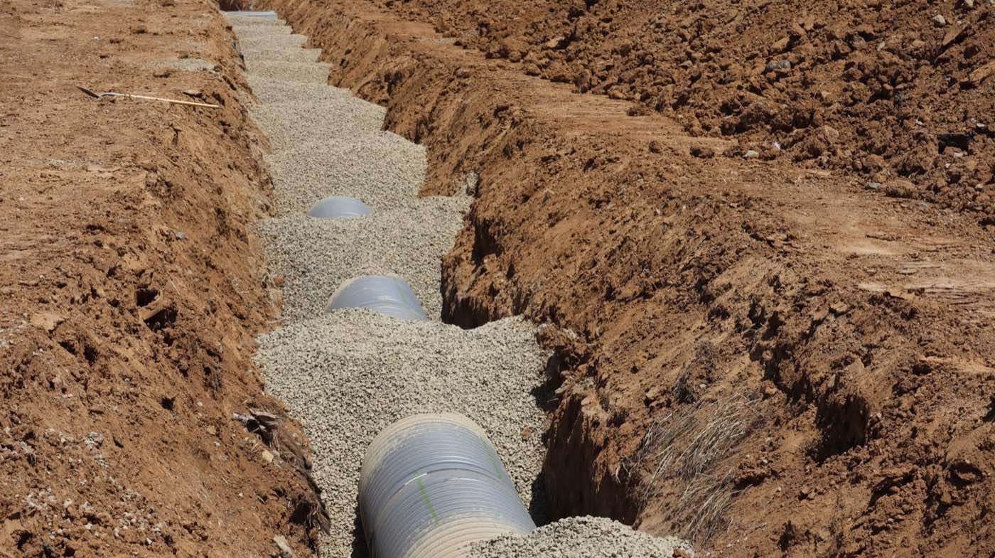 A perforated drain pipe laid in a gravel-filled trench